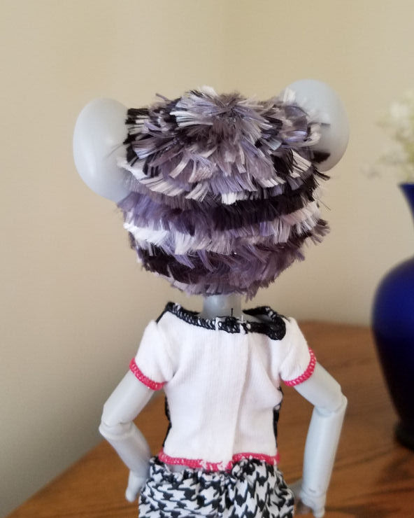 A grey Hujoo Phoebe Mouse doll standing facing away from the camera. She has a short hairstyle of choppy layers of patchy silver, steel grey, and black hair. The colors make a horizontal zebra striped sort of pattern.